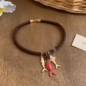 Detailed view of brown rope necklace with fish charms in red and golden finish