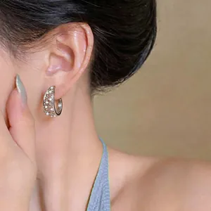 Close-up of elegant silver hollow C-shaped earrings with delicate pearls worn by a model