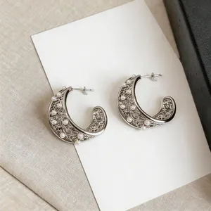 Close-up of intricate filigree C-shaped silver earrings accented with elegant white pearls
