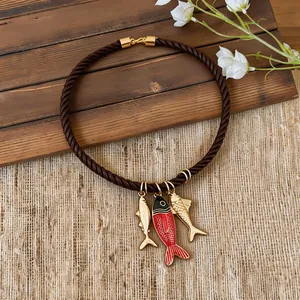 Detailed view of twisted rope necklace with red enamel and gold fish pendants