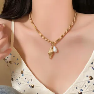 Close-up of a gold twisted chain necklace with shell and pearl pendants on a model