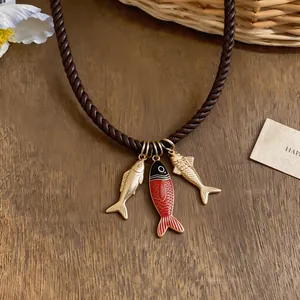 Detailed view of three enamel fish pendants on a stylish brown braided cord necklace