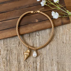 Macro view of gold twisted rope necklace with conch shell and teardrop pearl pendants