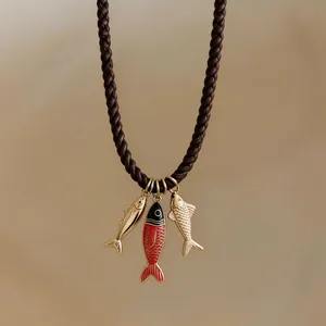 Detail view of a braided cord necklace with three decorative gold and enamel fish pendants.