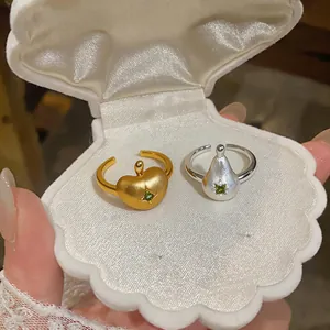 Gros plan de bagues pomme or et poire argent avec zircon vert dans un écrin coquillage