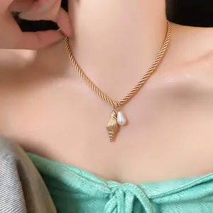 Close-up of a luxury gold rope chain necklace with shell and pearl pendants worn by a model.