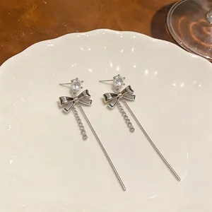 Detailed macro view of silver bow earrings with zircon studs and long tassels