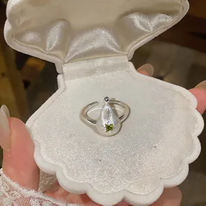 Gros plan d'une bague poire en argent brossé avec zircon vert dans une boîte en coquillage