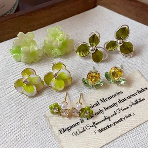 Close-up of various green flower and leaf stud earrings with zircons and pearls.