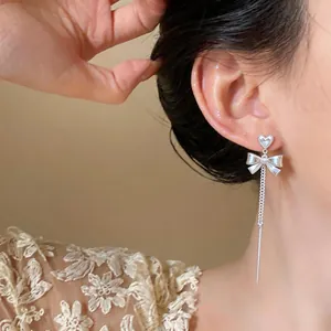 Detail view of silver heart stud earrings with zircon bow and long tassel chain