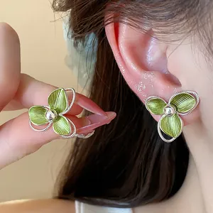 Detailed macro view of elegant green three-petal flower stud earrings worn on model's ear