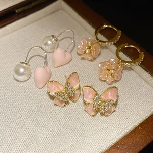Close-up of pink enamel butterfly studs, heart pearl hooks, and floral earrings in a box