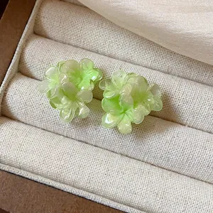 Close-up of elegant green resin flower stud earrings on a beige jewelry display tray