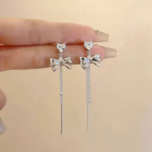 Close-up view of silver bow-knot tassel earrings featuring sparkling heart zircon details