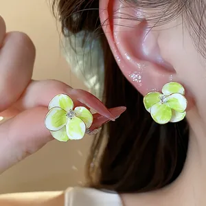Macro close-up detail of 18k gold plated flower stud earrings with green petals and zircon