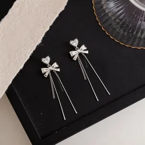 Detail of silver bowknot earrings featuring zircon heart studs and long tassels.