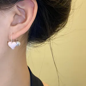 Detail shot of a pink oil-drop heart and pearl earring worn on the ear
