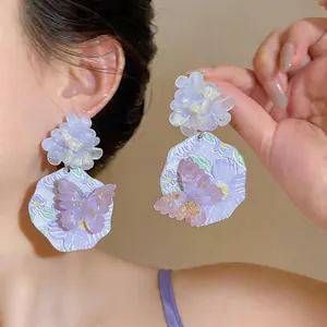 Dettaglio ravvicinato di orecchini a fiore e farfalla in resina viola su una modella