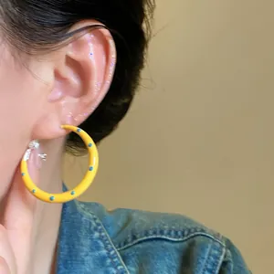 Primo piano di una modella con orecchini a cerchio gialli a pois e giacca di jeans
