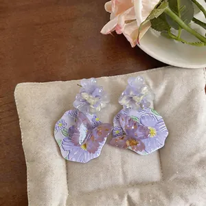 Dettaglio di orecchini a fiore in resina viola con farfalla e accenti di foglia d'oro