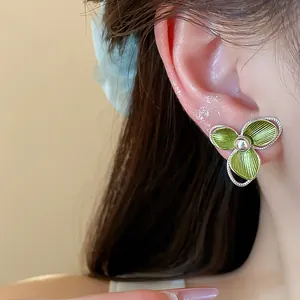 Close-up detail of a delicate green flower stud earring with 18k gold plating worn on ear model.