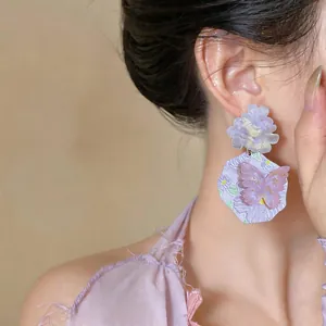 Dettaglio di orecchini a fiore in resina lavanda stile coreano con farfalla sulla modella.
