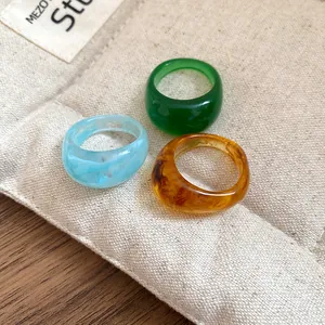 Lot de trois bagues colorées en résine épaisse verte ambre et bleue sur sac en toile