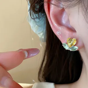 Close-up of heart zircon flower stud earring on ear with green and yellow stones.
