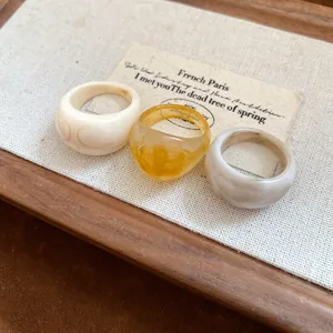 Vue détaillée d'un ensemble de bagues en résine minimalistes en blanc, ambre et gris.