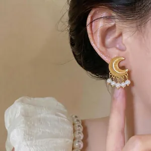 Elegant vintage gold crescent moon earrings with pearl tassels shown on a model's ear