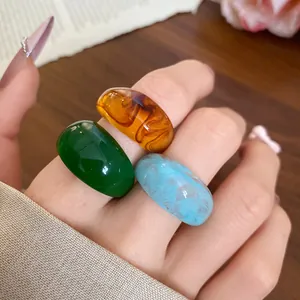 Gros plan détaillé de trois bagues en résine élégantes aux motifs vert, ambre et bleu.