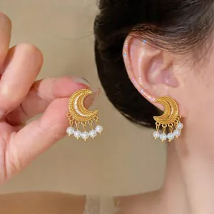 Close-up detail of vintage gold moon earrings with elegant pearl tassels worn on a model's ear.
