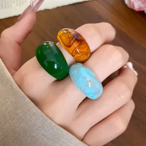 Gros plan de trois grosses bagues colorées en résine verte, ambre et bleu clair.