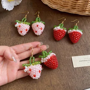 Detailed view of handmade red and pink beaded strawberry earrings on wooden surface.