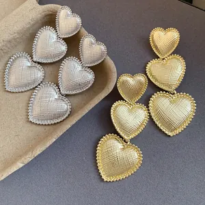 Detailed view of textured triple heart-shaped drop earrings in gold and silver finish