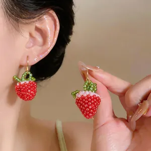 Close-up detail of handmade red strawberry glass bead earrings with gold hooks