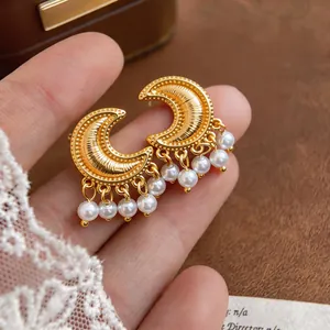 Close-up of vintage gold crescent moon earrings with elegant pearl tassels held in hand