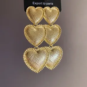Close-up of gold pleated heart tassel earrings with intricate metallic texture.