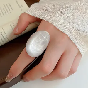 Close-up view of a chunky oval pearl-white resin ring worn on a finger with aesthetic props