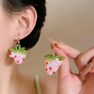 Close-up of cute pink beaded strawberry earrings with gold hooks shown on an ear