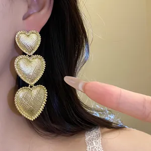 Close-up of gold textured three-tier heart drop earrings with pleated surface detail
