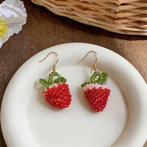 Detailed macro view of handmade red beaded strawberry hook earrings on a white plate.