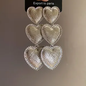 Macro detail of silver-colored wrinkled heart earrings with textured finish and beaded edges