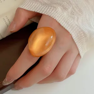 Detailed view of an oversized orange resin ring with a shimmering cat-eye effect