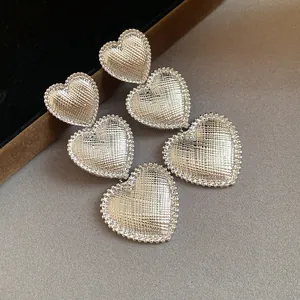 Macro view of textured silver-tone triple heart drop earrings on a neutral background
