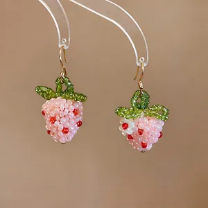 Close-up of handmade pink beaded strawberry earrings featuring delicate green leaf details.