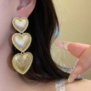 Close-up of elegant gold pleated heart drop earrings with textured finish on model