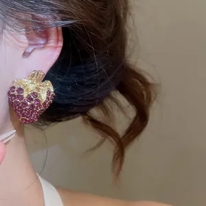 Detailed view of a vintage style gold-tone rhinestone strawberry stud earring on an ear