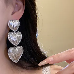 Elegant macro view of three-tier textured silver heart drop earrings worn on a model's ear.