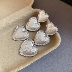 Detailed close-up showing textured silver heart dangle earrings with beaded edges on a rustic base
